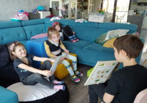 w domu chłopiec siedzi przed trzema dziewczynkami na niebieskiej kanapie i pokazuje książkę